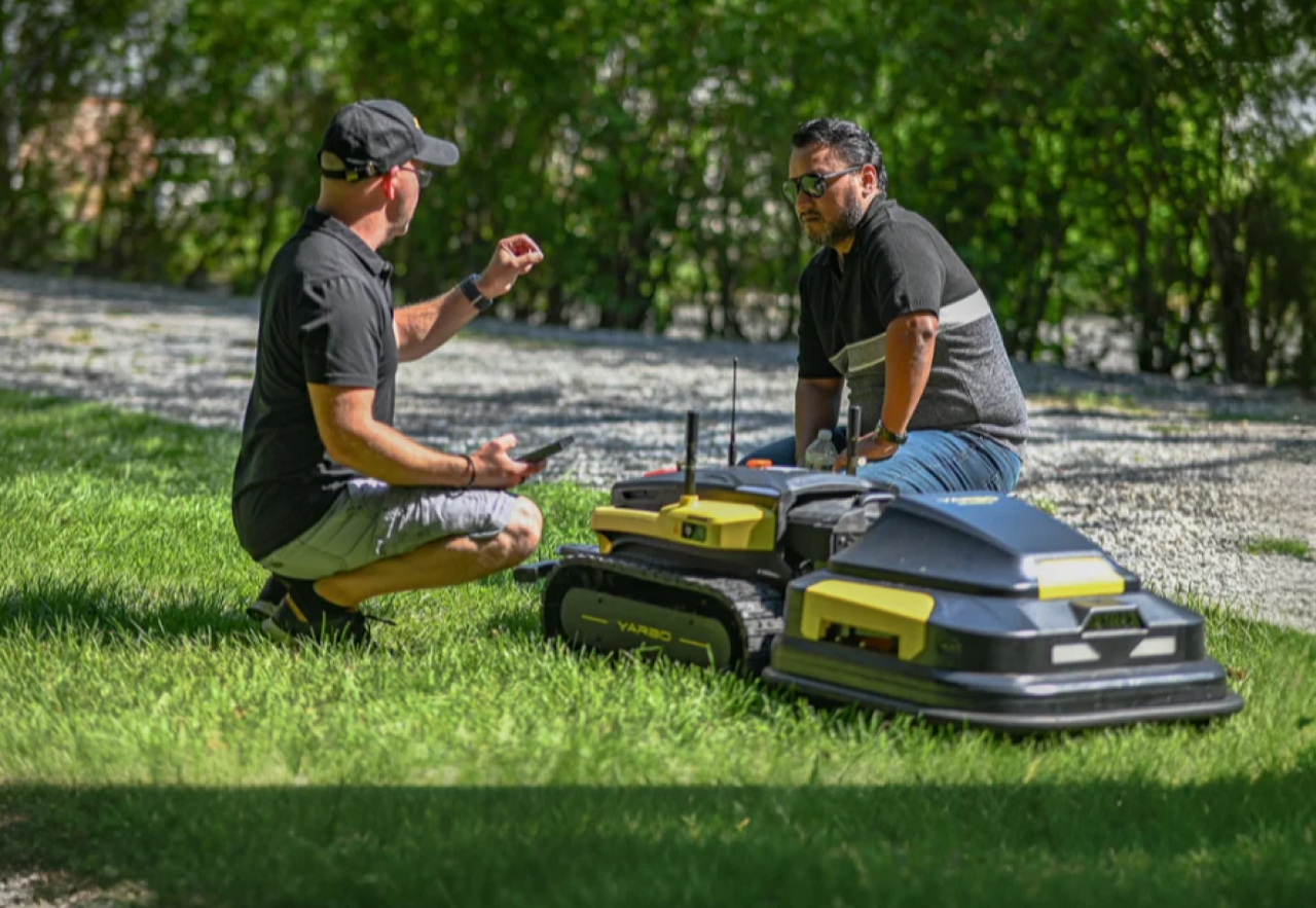 Two users inspecting and discussing Yarbo lawn mower on a grass lawn during setup