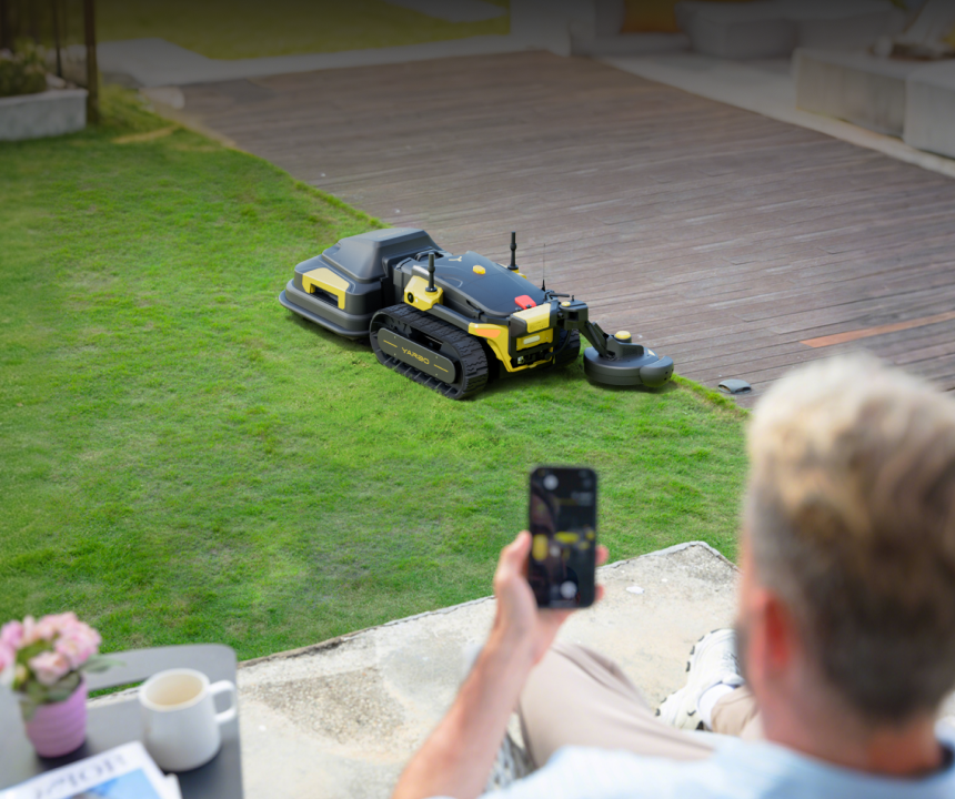 A house owner using a smartphone to control a Yarbo Blower in a grassy area.