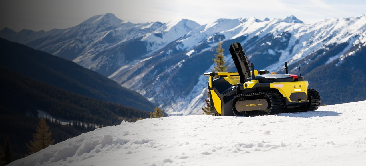 Yarbo snow blower operating in deep snow with a mountain winter landscape backdrop